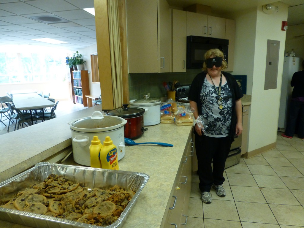 Woman wearing sleepshades stands beside a row of hotel pans filled with food