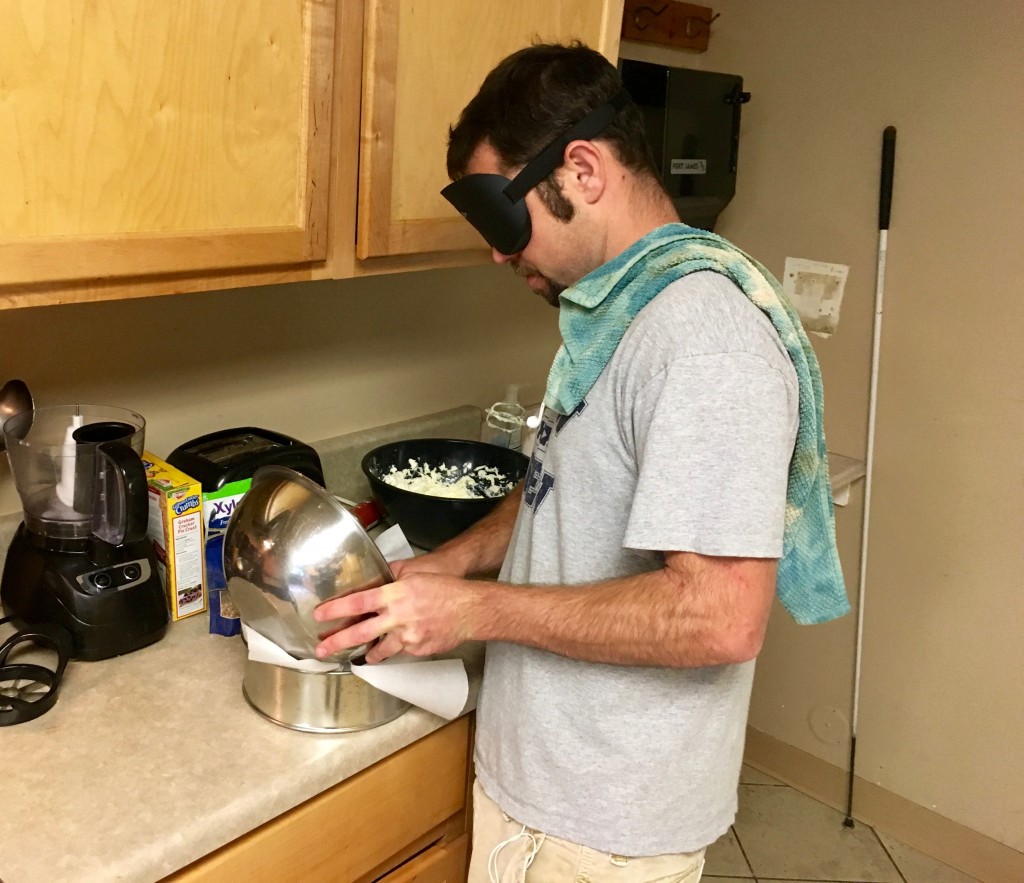 A trim man with dish towel over his shoulder pours a thick white mixture from a bowl to a pan