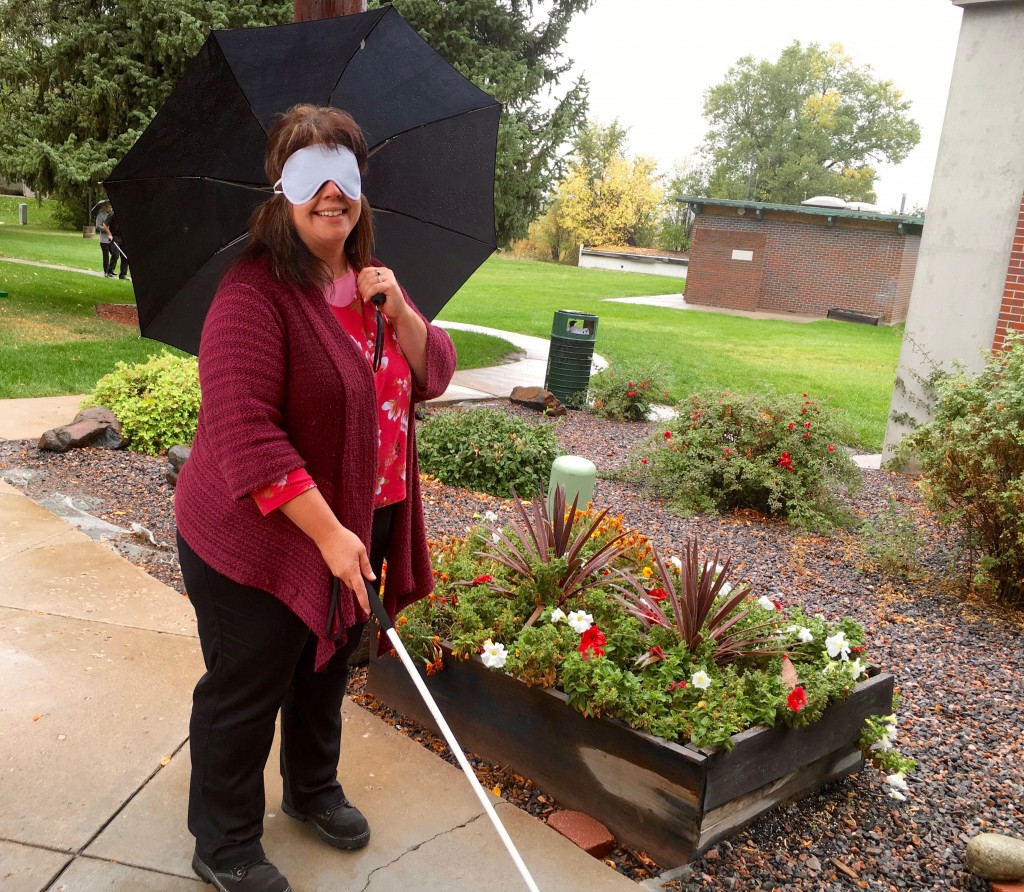 A woman wearing sleep shades returns to the Center with her white cane in one hand and umbrella in the other