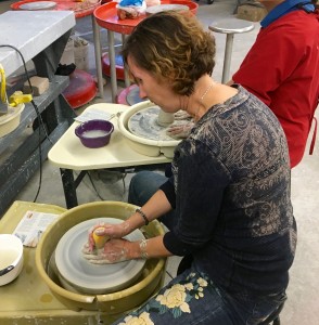 a woman holds a wet sponge against her spinning clay, her other hand stabilizes the base