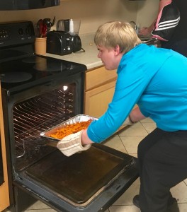 A young man stoops to take a large hotel pan of fries from a hot oven