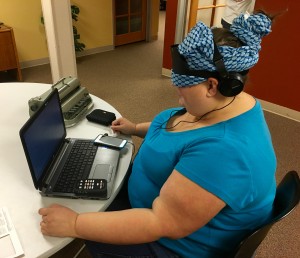 Woman sits at a table working with laptop, iPhone and Stream.