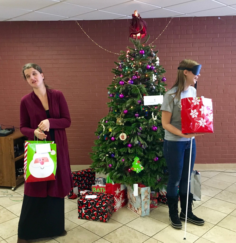 Two young women manage gifts beneath a lighted tree