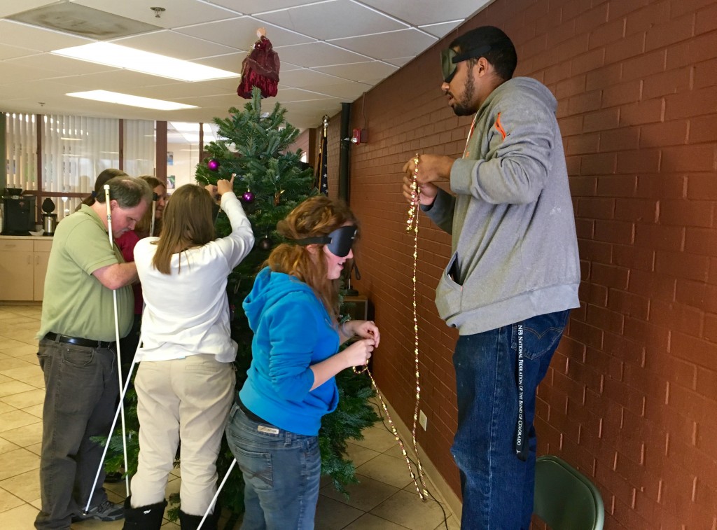 Six people surround a Christmas tree, adding decorations.