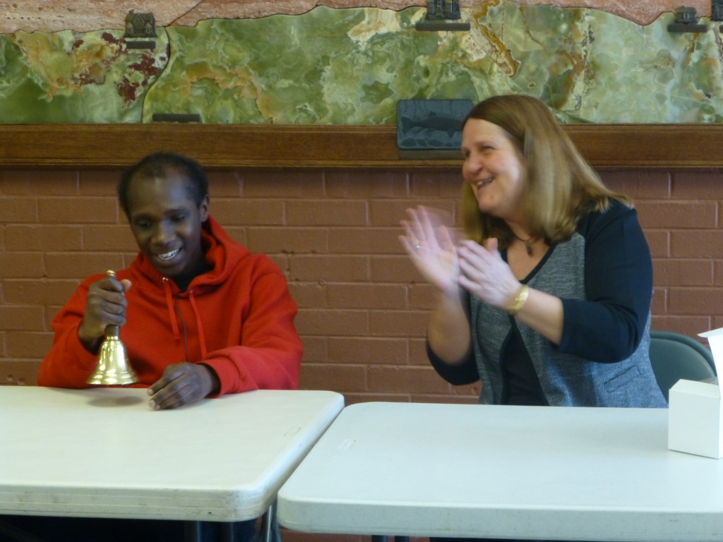 a seated young man smiles as he holds his bell