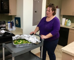 a woman pushes a cart with a large tray filled with Brussels sprouts