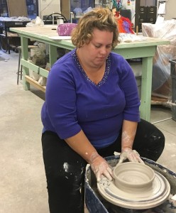 a woman at a potter's wheel puts final touches on her wet clay