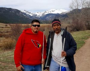 Two men grin at the camera with snowy mountains behind them