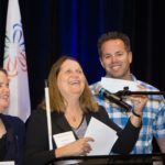 Marc Greytak presents check to Julie Deden at podium, Maryann Migliorelli looks on