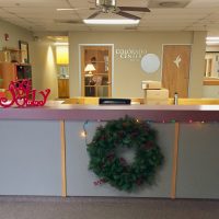 A wreath hanging on the front desk, Christmas lights and wooden ornaments - a Christmas Tree and the word Jolly
