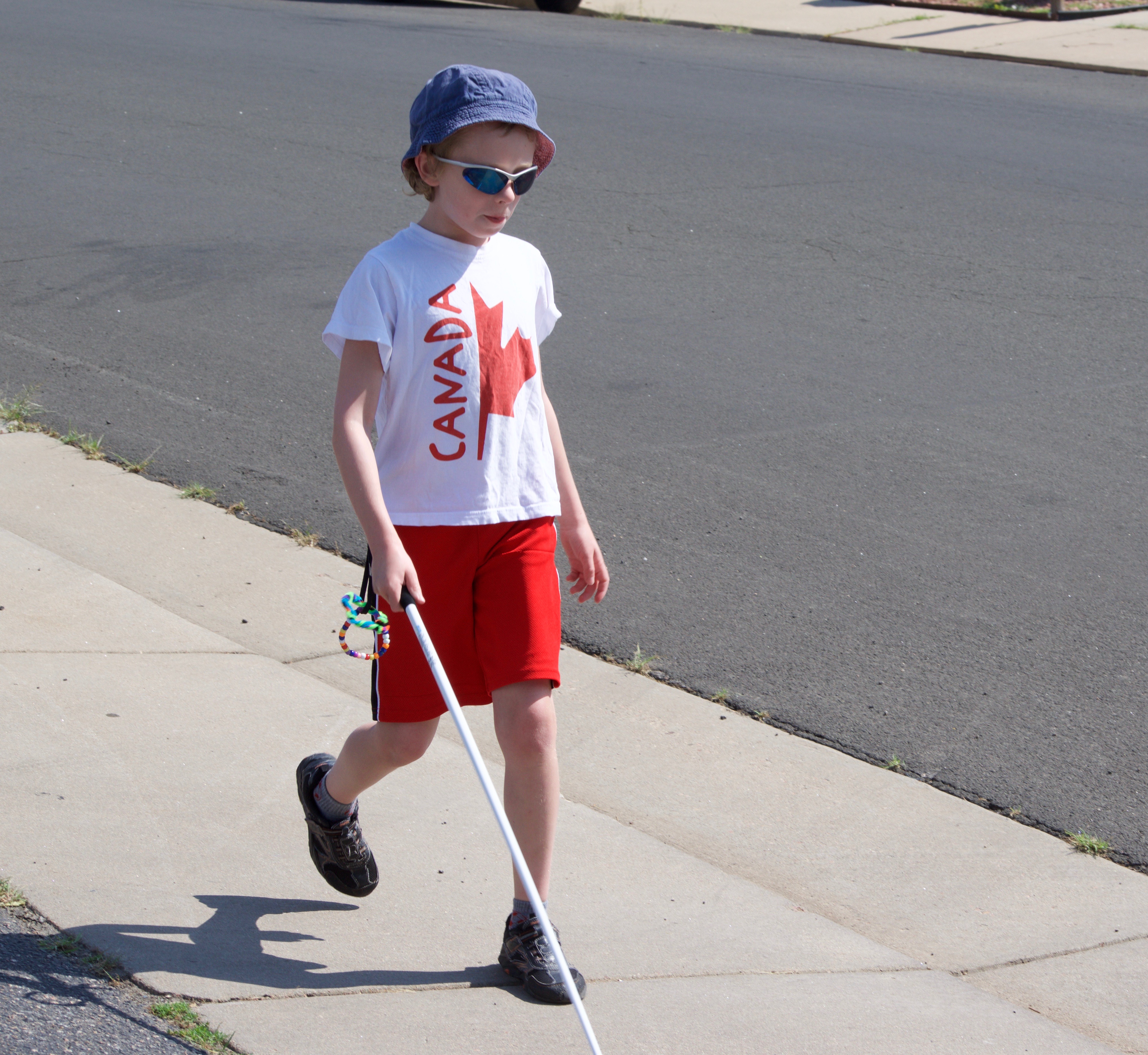 A young boy walking along the sidewalk using his white cane