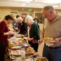 Looking down the line at the food table at the Senior Christmas Party - Anahit is serving and Gary is holding a a nice plate full of goodies