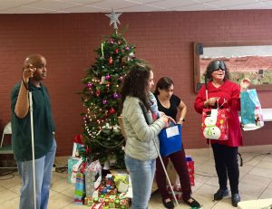 Shon and CC in line to open gifts, Carrina and Blanca pass them out beside the lighted tree