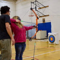 Courtney in sleepshades holding bow gets tips from NSCD's Mike 