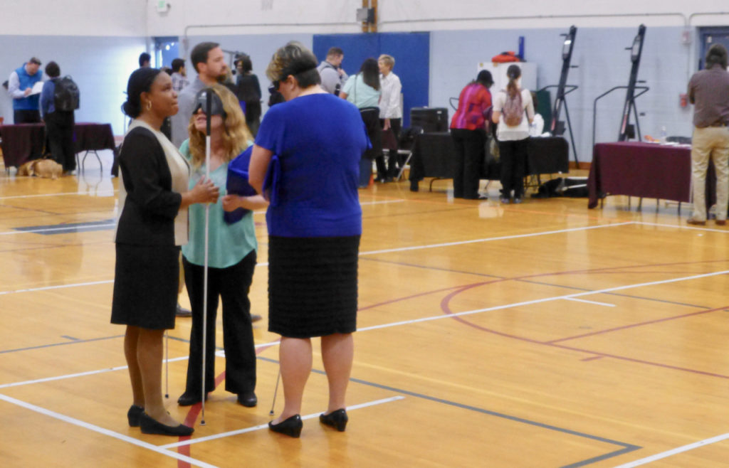 Three smartly-dressed women chat in a large, busy gym