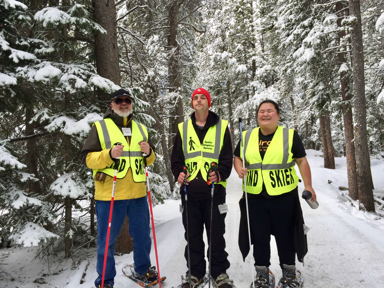 Five people wearing snow shoes on a wintery forested path with snow covered branches.