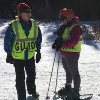 Ellen with ski poles and snowshoes next to her guide on the slope