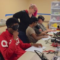 Leon, Jay ,and J.D. look at a tactile schematic diagram while a volunteer points out specific features