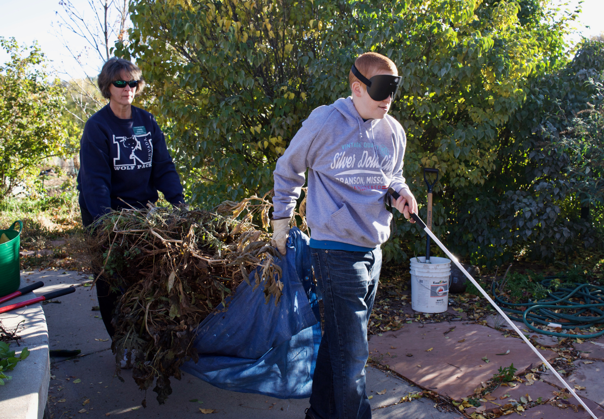 Tyler leads the way as he and Master Gardener Barb carry a tarp loaded with stems and leaves to the dumpster