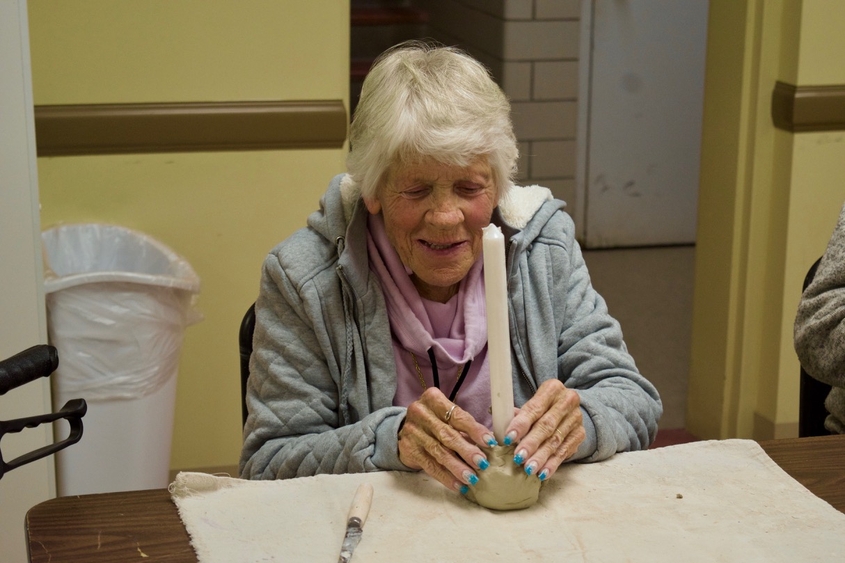 Judi fits a tall white candle into a clay base she is shaping into a candle holder