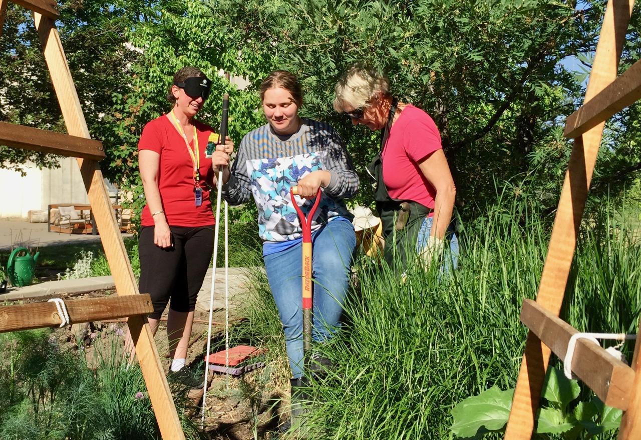 Amber turns dirt over in the garden with Annette and Master Gardener Barb