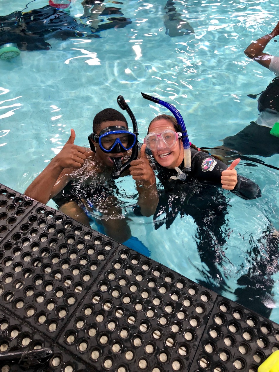 A young man in diving mask and snorkel gives the thumbs up after surfacing with his instructor