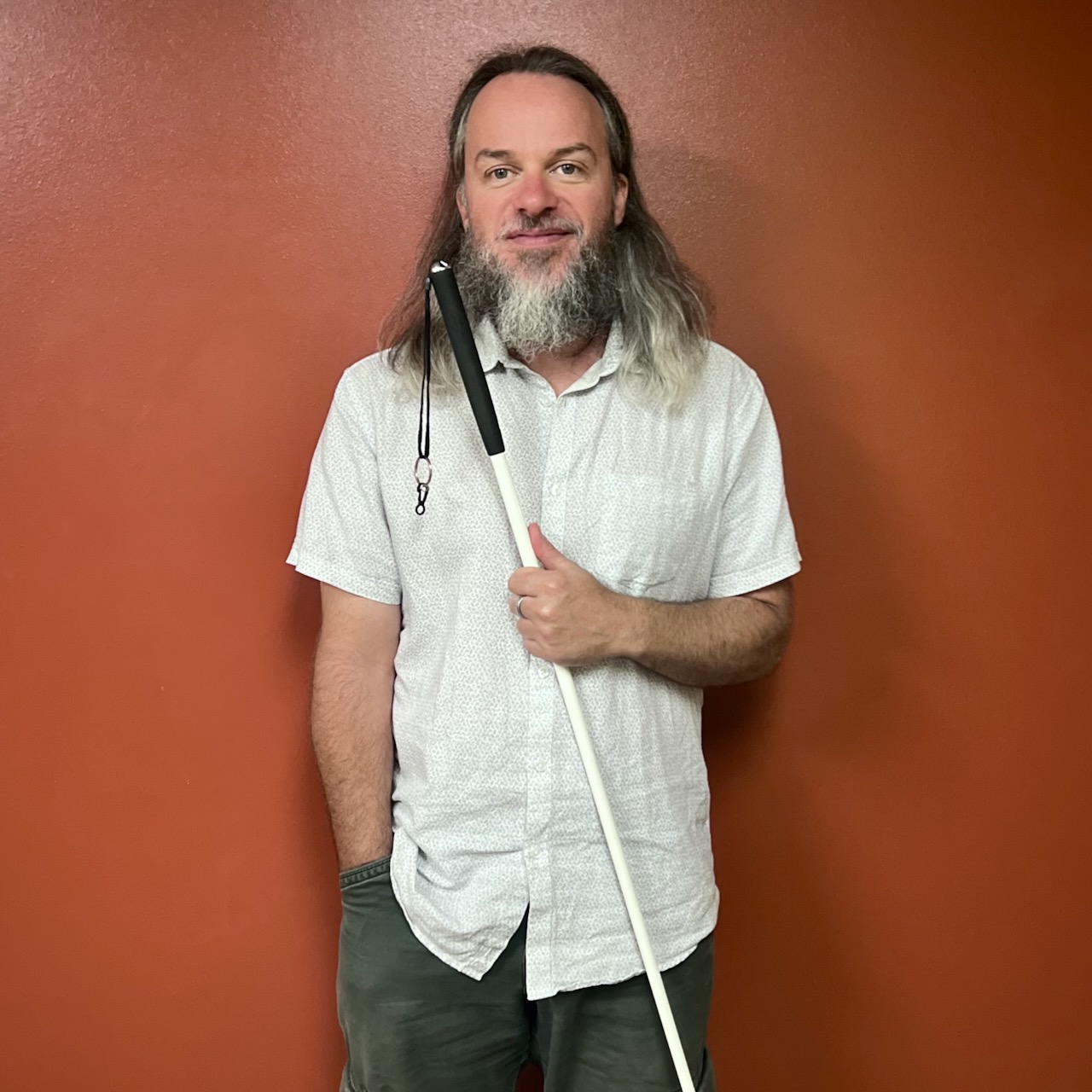 Jeremy Smith standing with his white cane against a rust colored wall