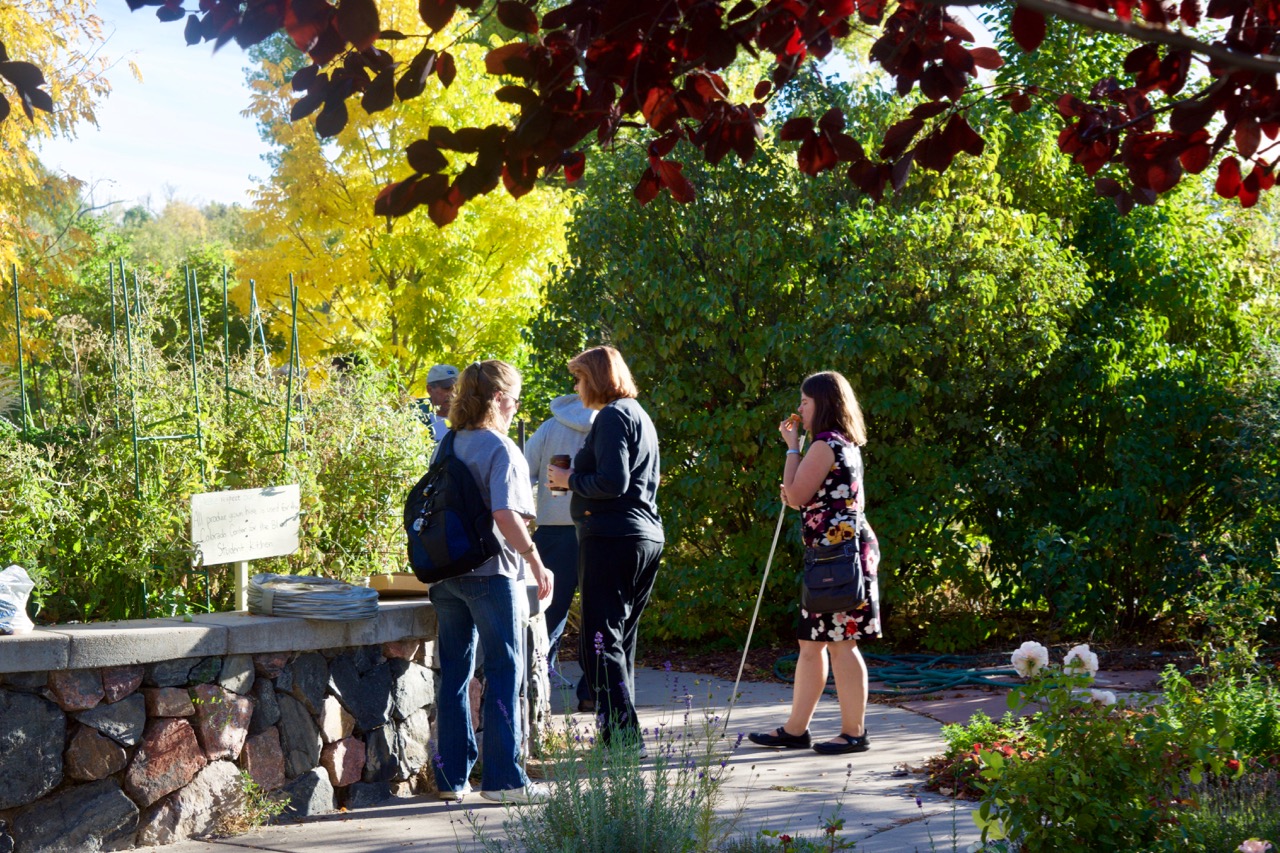 Large group of students interacts with the Master Gardeners against a wall of Fall colors
