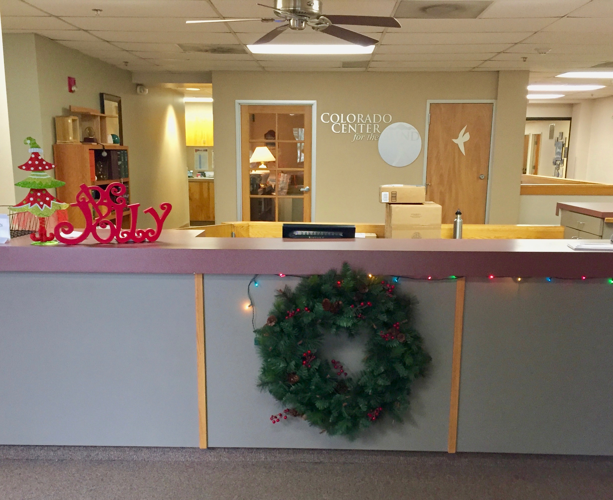 A wreath hanging on the front desk, Christmas lights and wooden ornaments – a Christmas Tree and the word Jolly