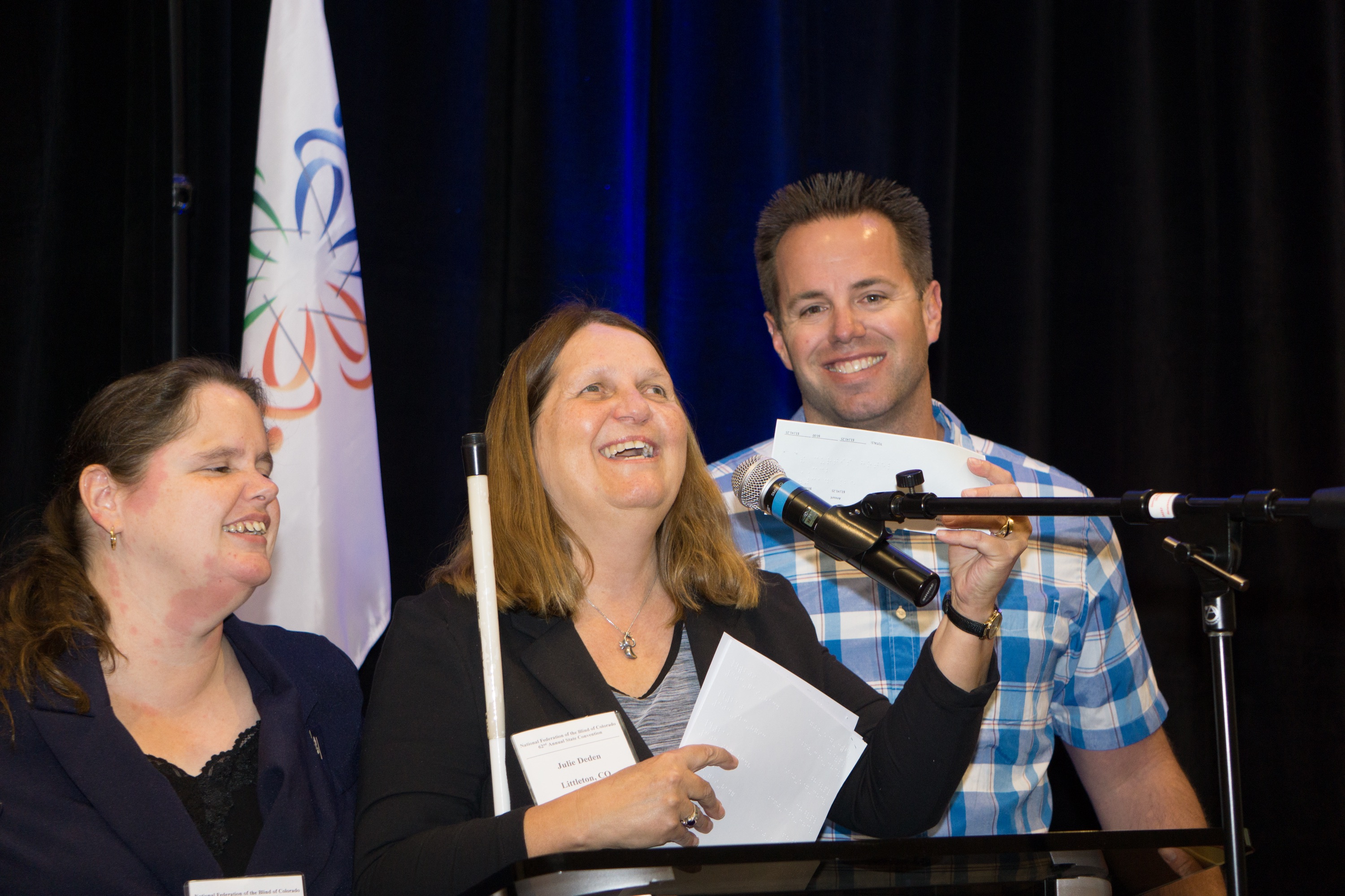 Marc Greytak presents check to Julie Deden at podium, Maryann Migliorelli looks on