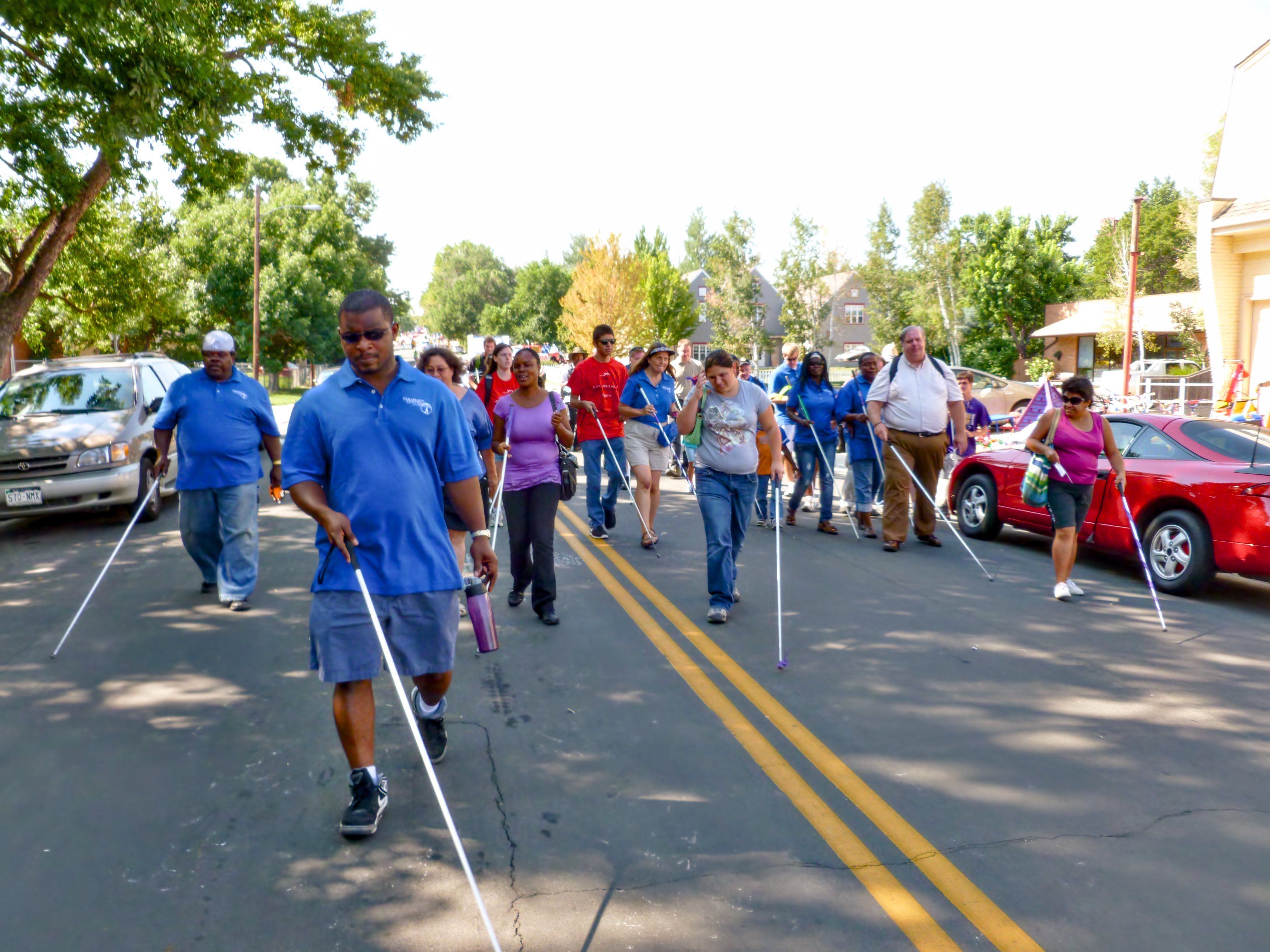 a group of people carrying white canes walk down the middle of a street