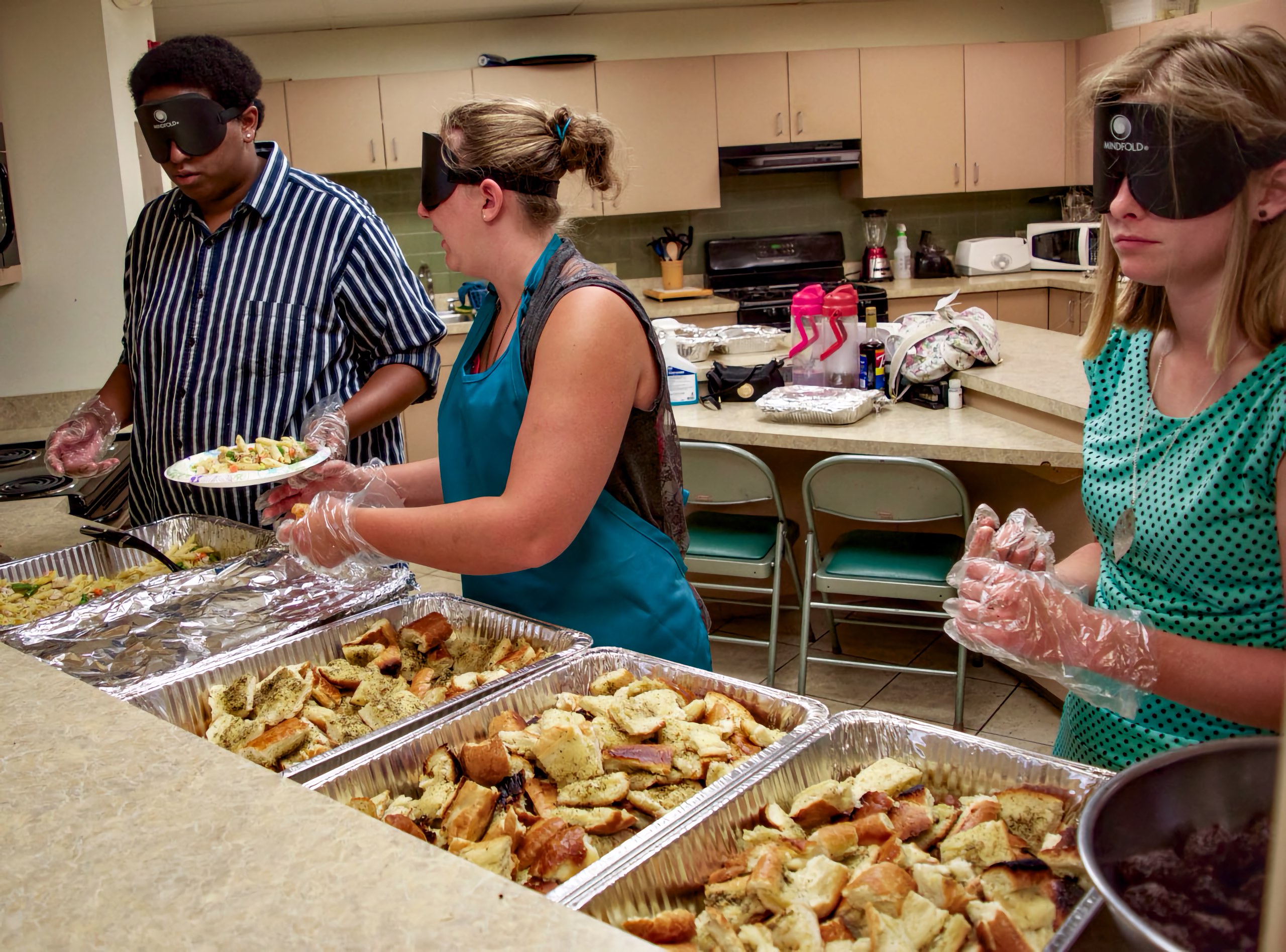 Three students inside a serving window, each serving from a different pan of food