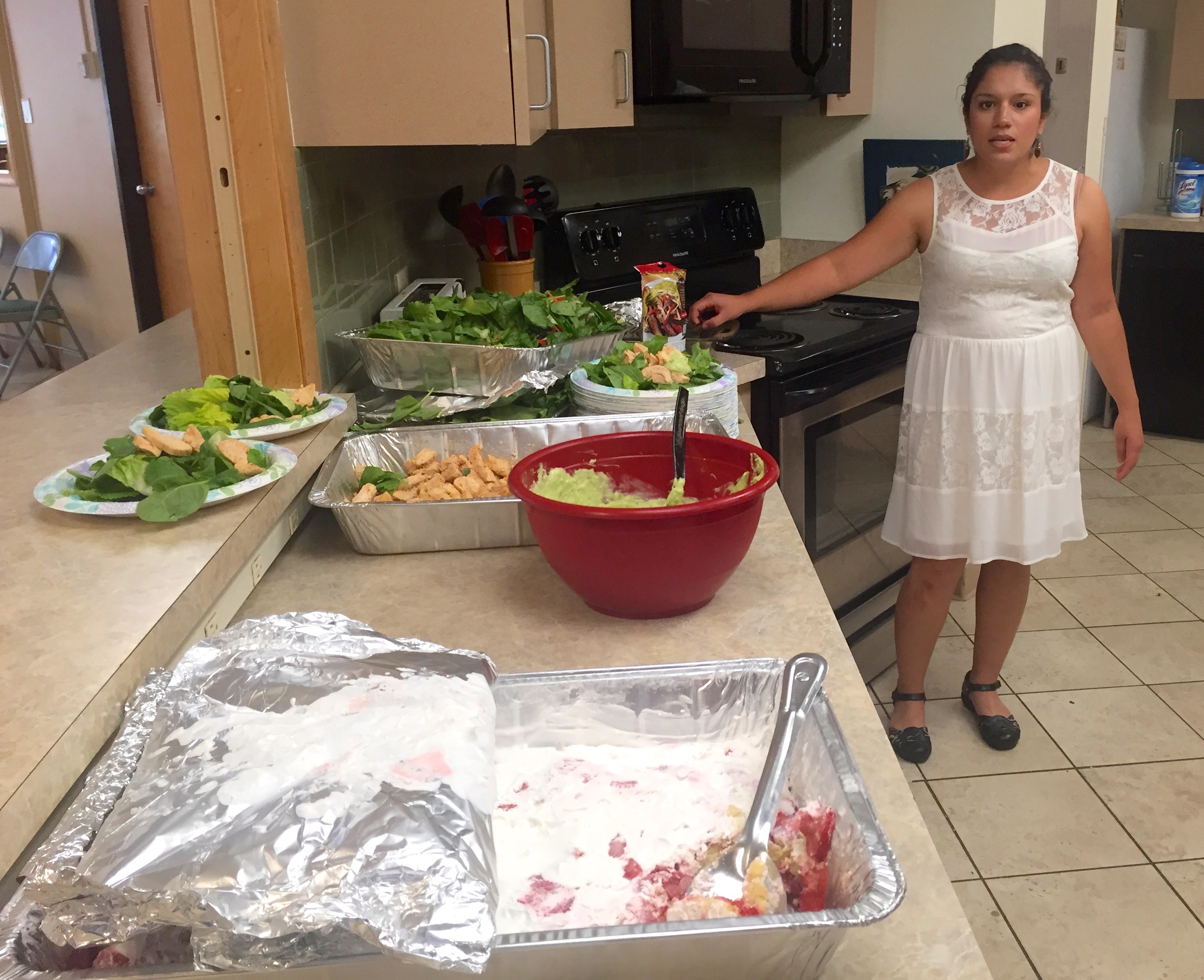 Looking down the serving area over all the trays of food as Cindy stands at the far end describing what she prepared