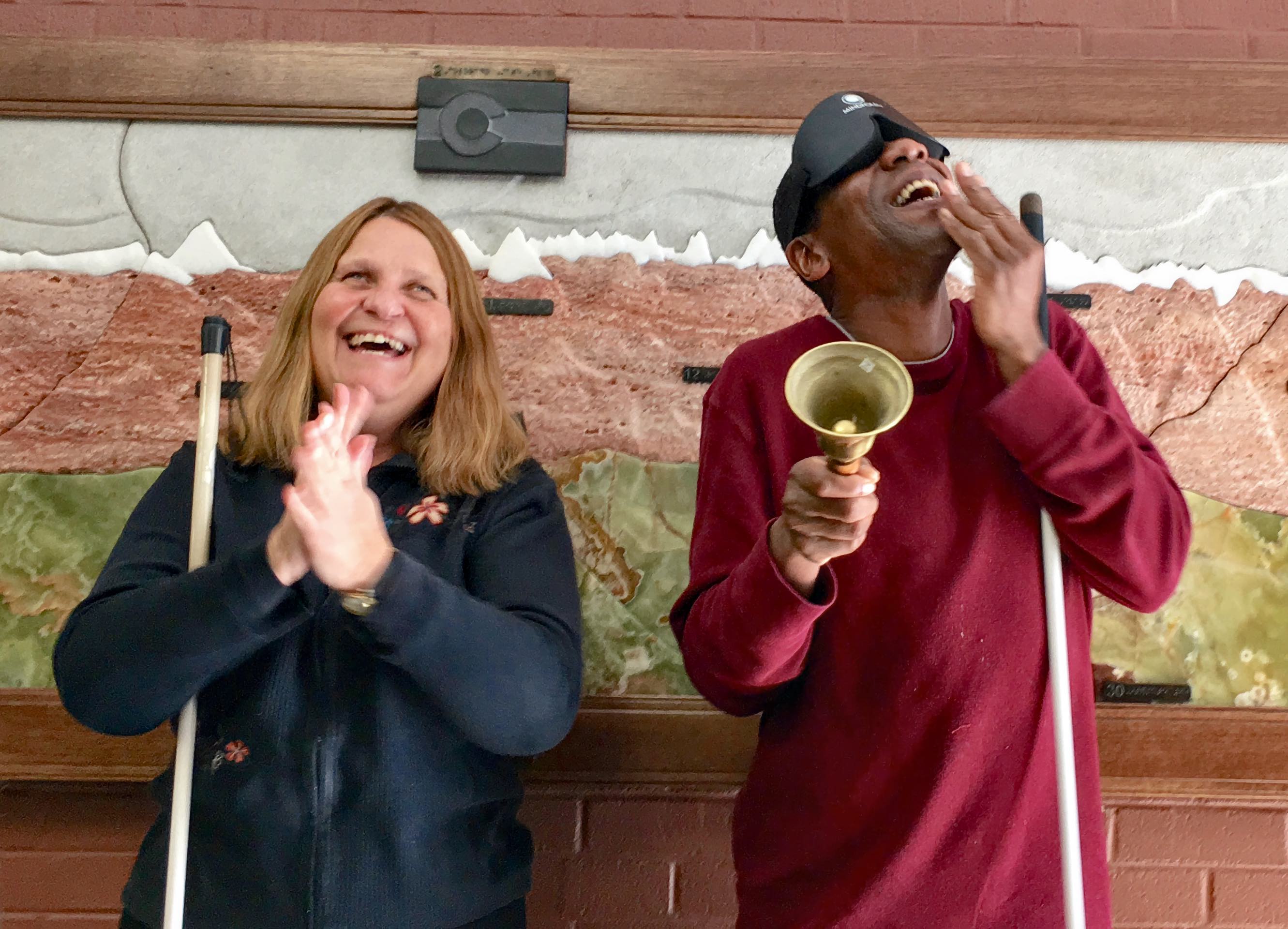 A man rings his bell with a wide grin while a woman applauds