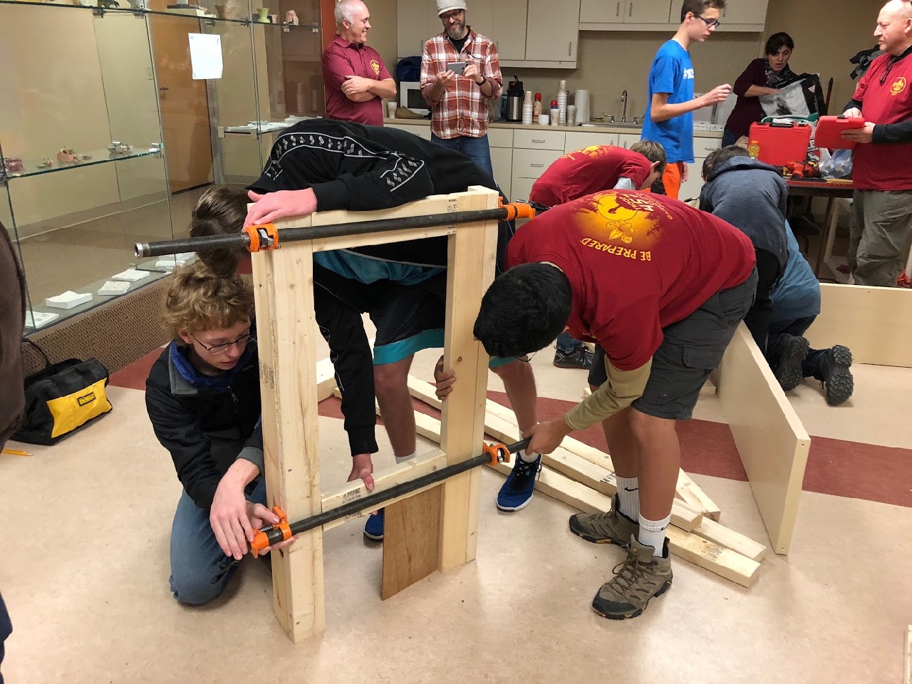 Devin, Bobby and Kevin use large pipe clamps to hold the pieces together and square one set of legs for a workbench they are building