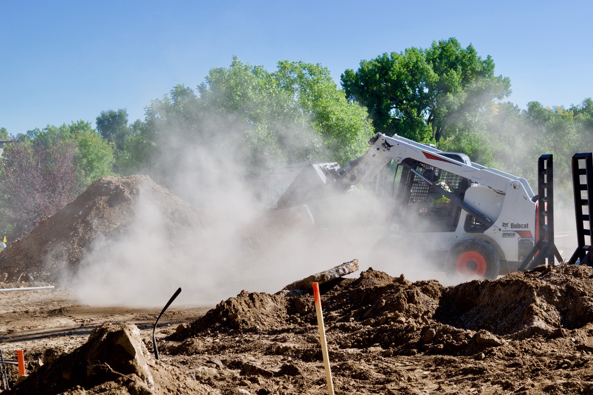 Dust clouds swell around a front-end loader moving dirt and debris during parking lot construction.