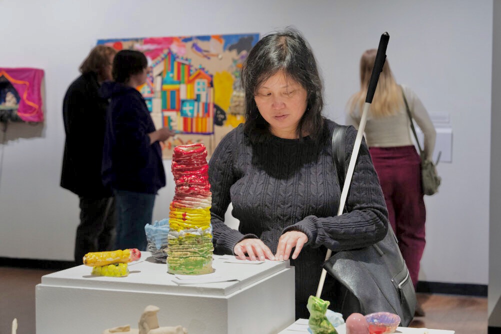 an Asian woman holding a white cane examines colorful ceramics.