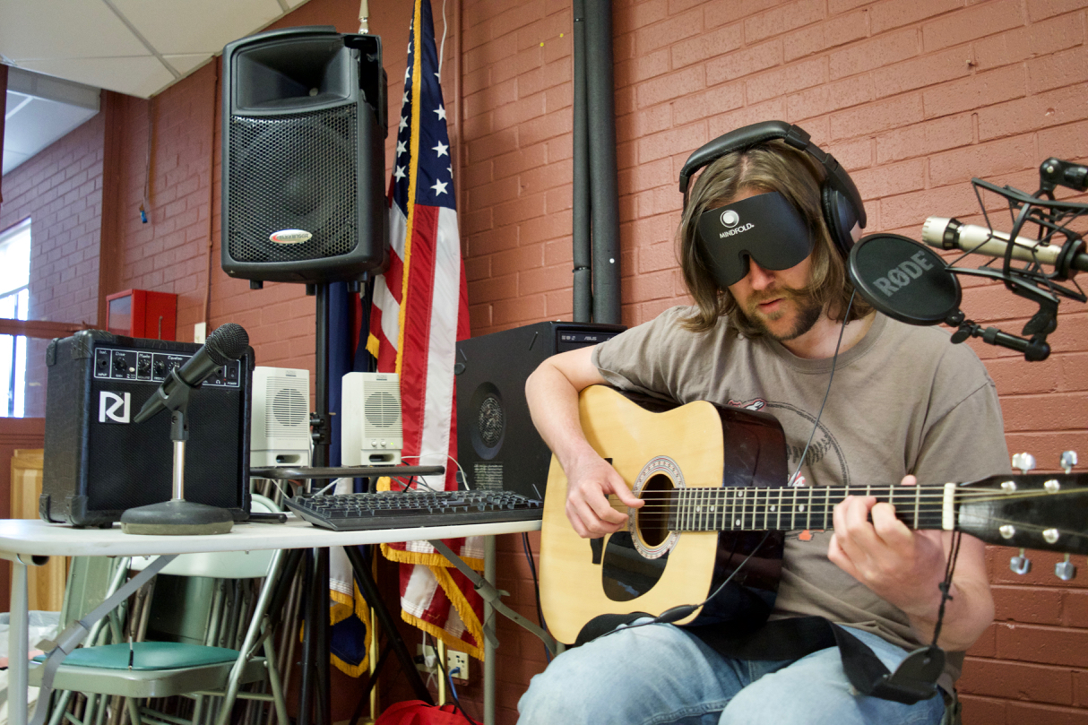 Graham in headphones before the mic and mixing board, laying down a guitar track