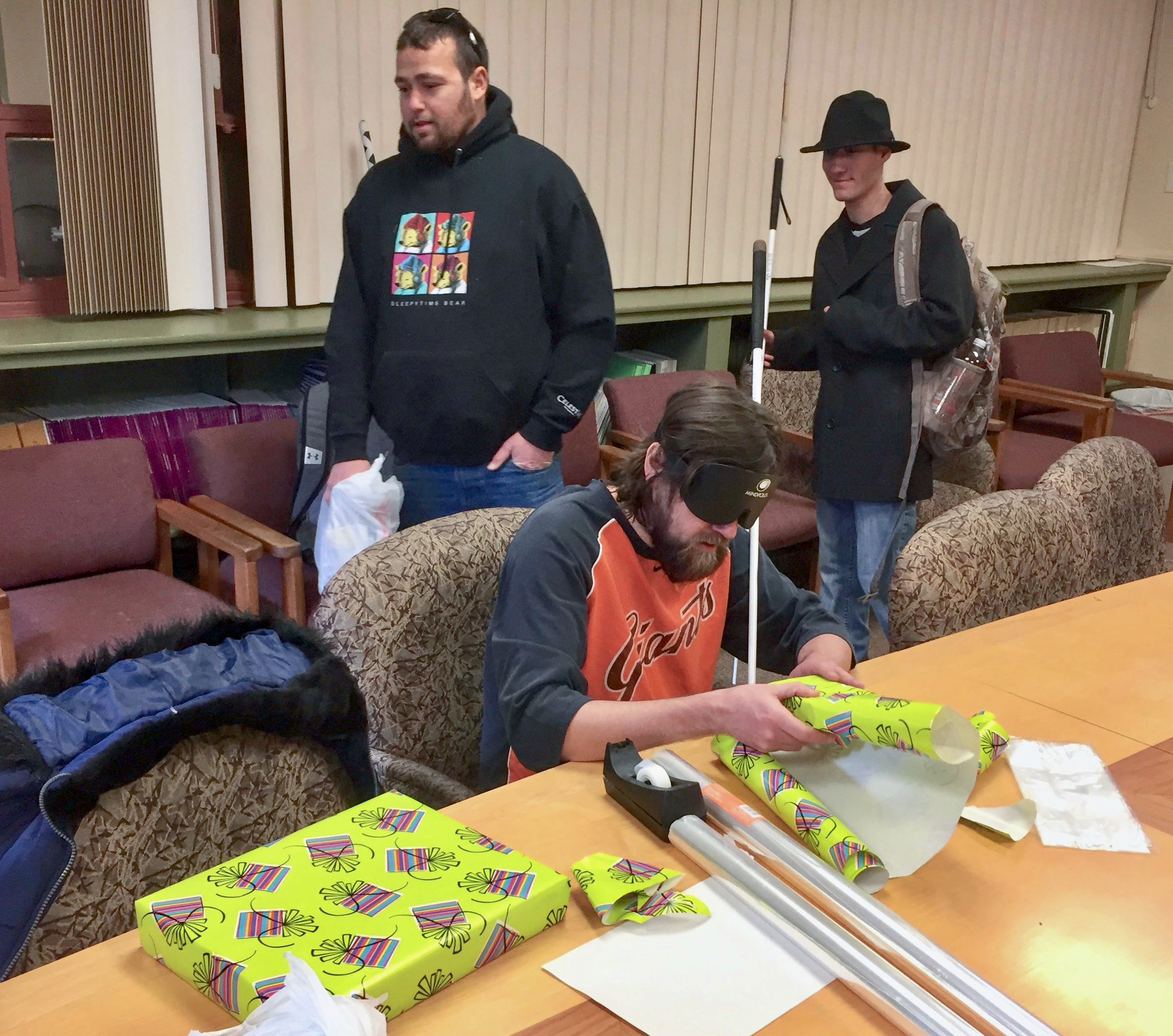 Graham wraps a gift with Chris Perez and Jackson walking in to do the same