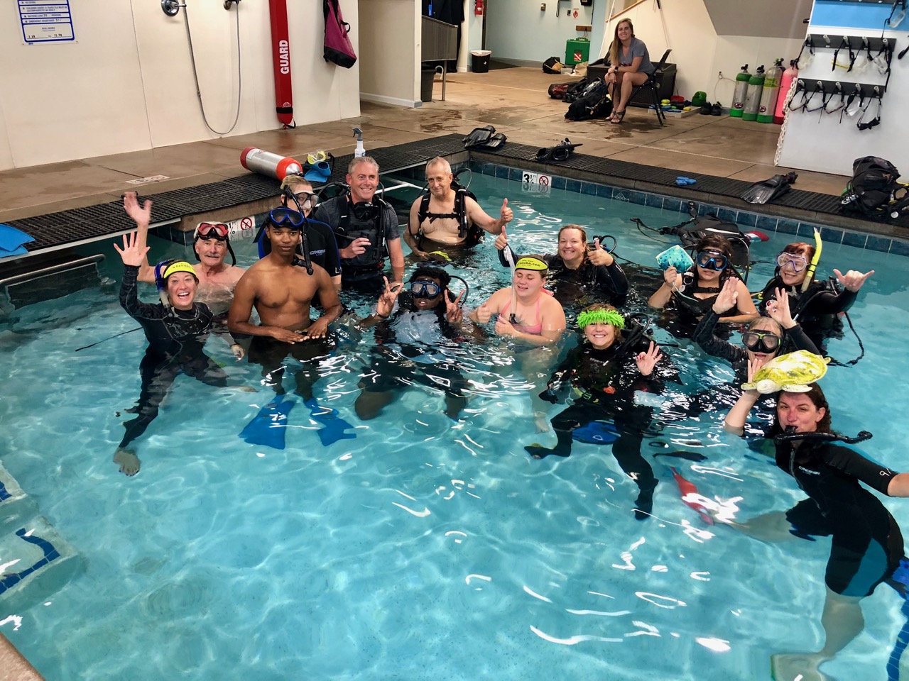 Group of 14 in Scuba Gear in the corner of the pool smile and wave