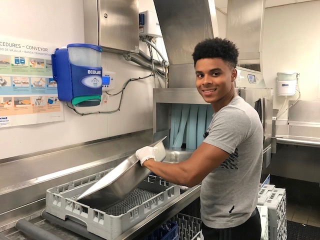 Kameron runs a large hotel tray through a commercial dish washer