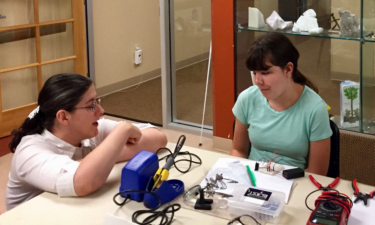Jamie talks to Maddie while she works with components on a breadboard