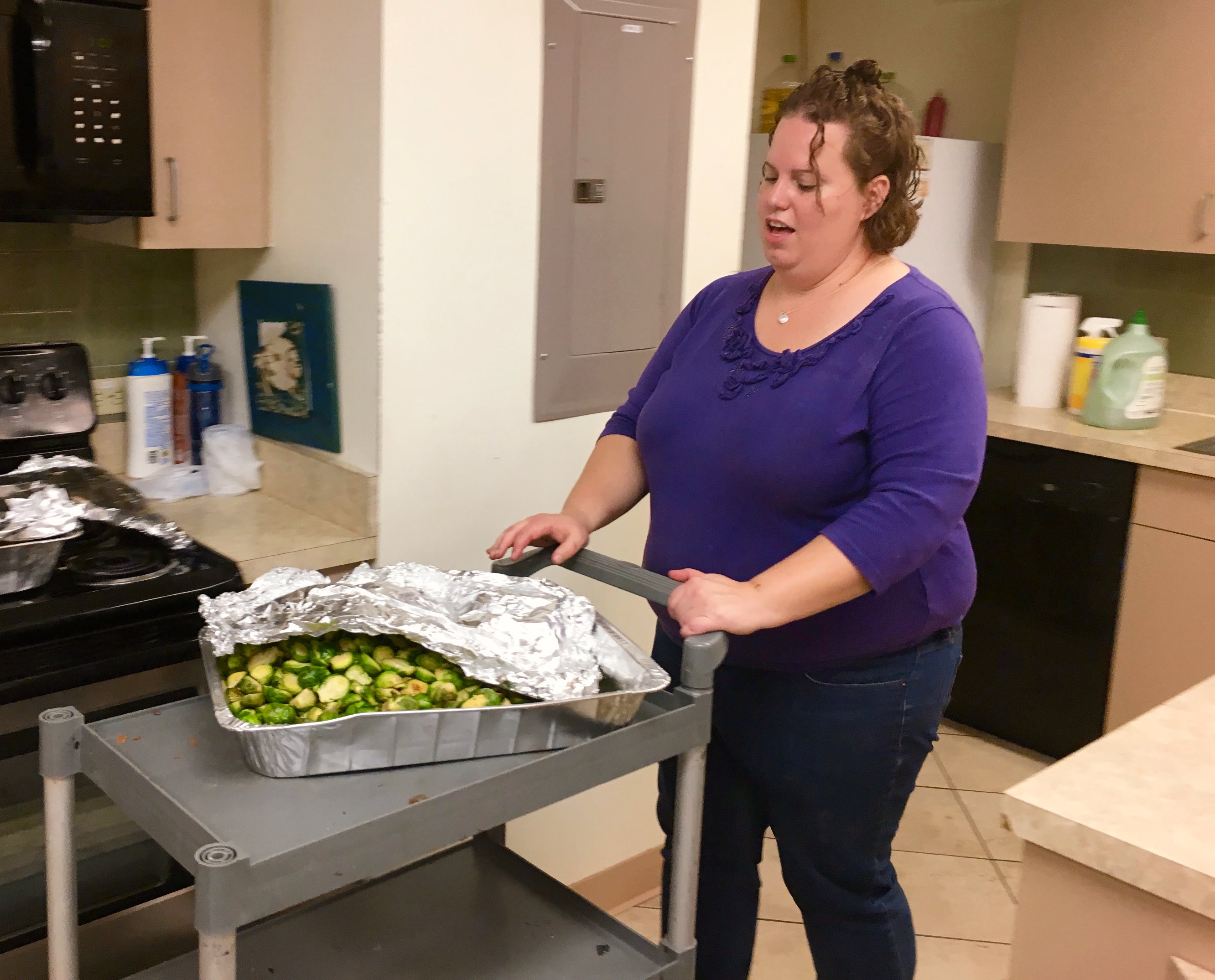 a woman pushes a cart with a large tray filled with Brussels sprouts