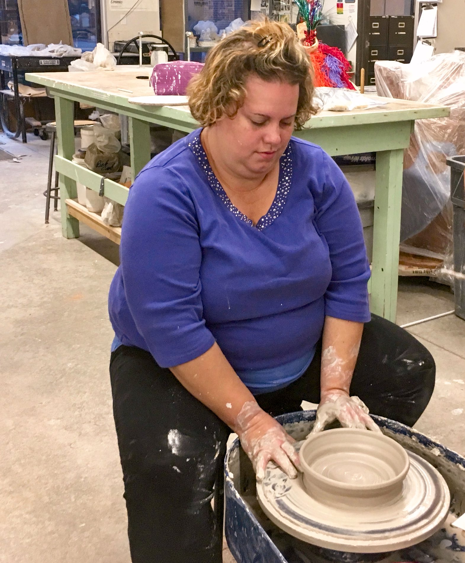 a woman at a potter's wheel puts final touches on her wet clay