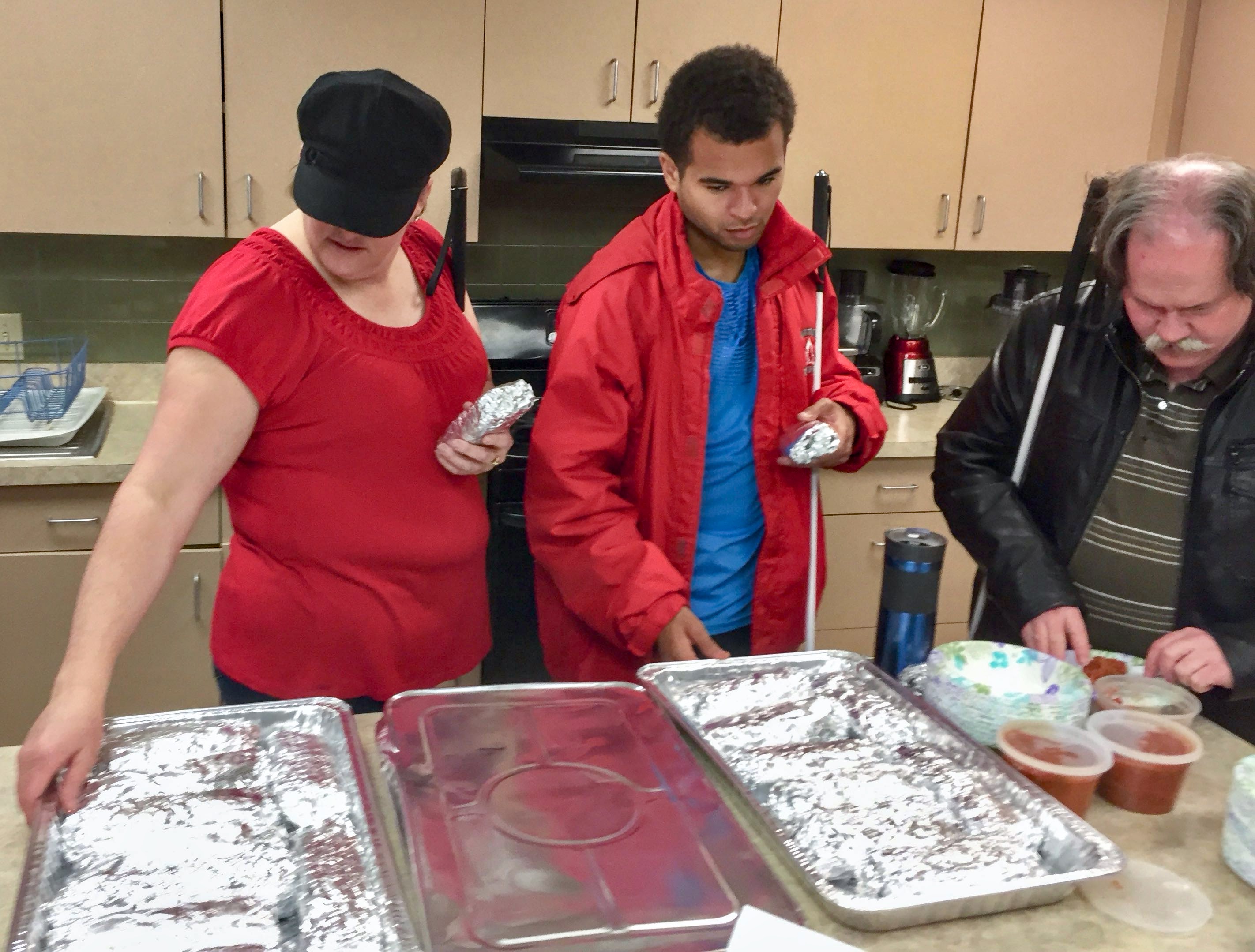 Libby, Chaz and Chip get breakfast burritos out of huge trays in the large kitchen
