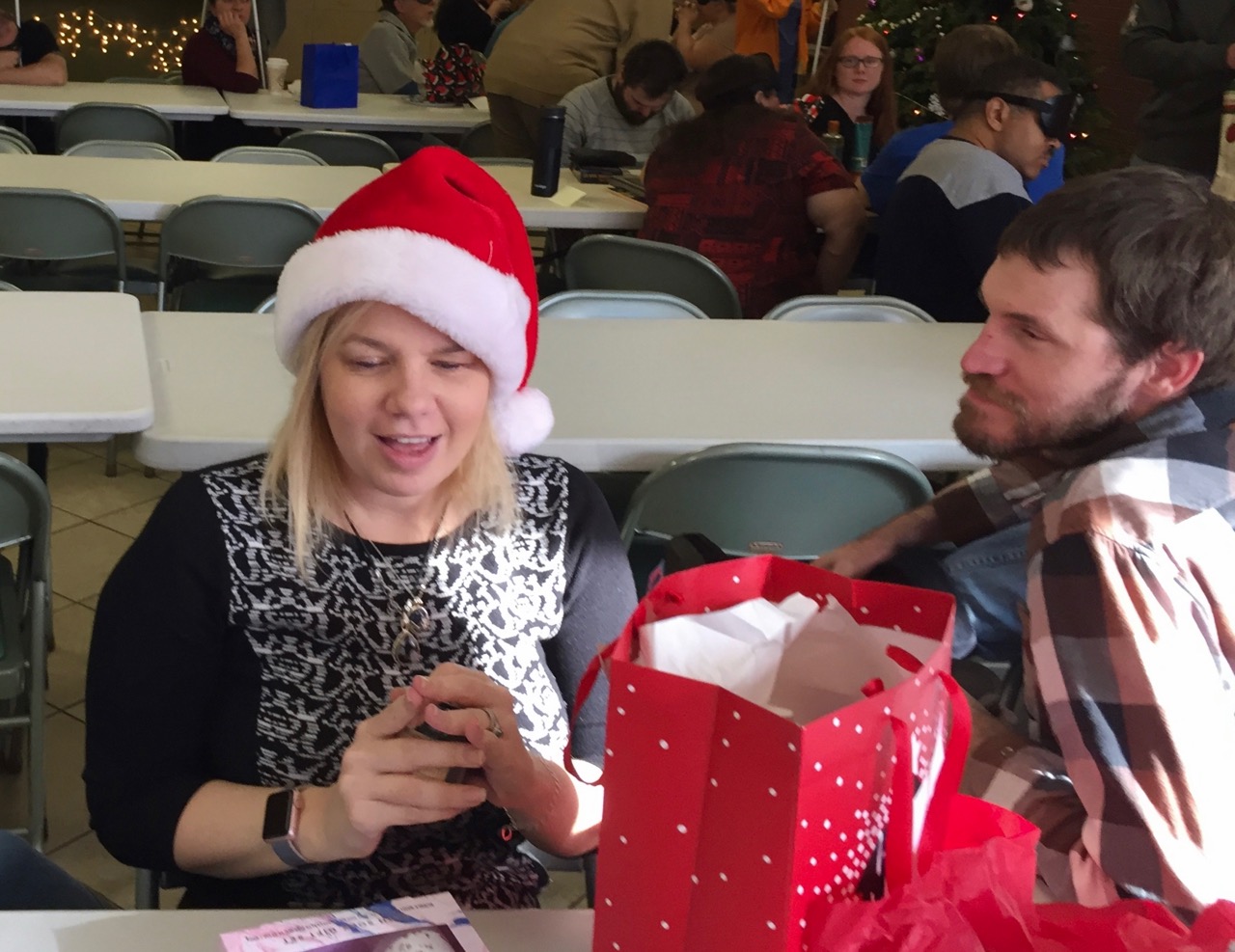 Maureen wearing her Santa hat opens her gift while David looks on