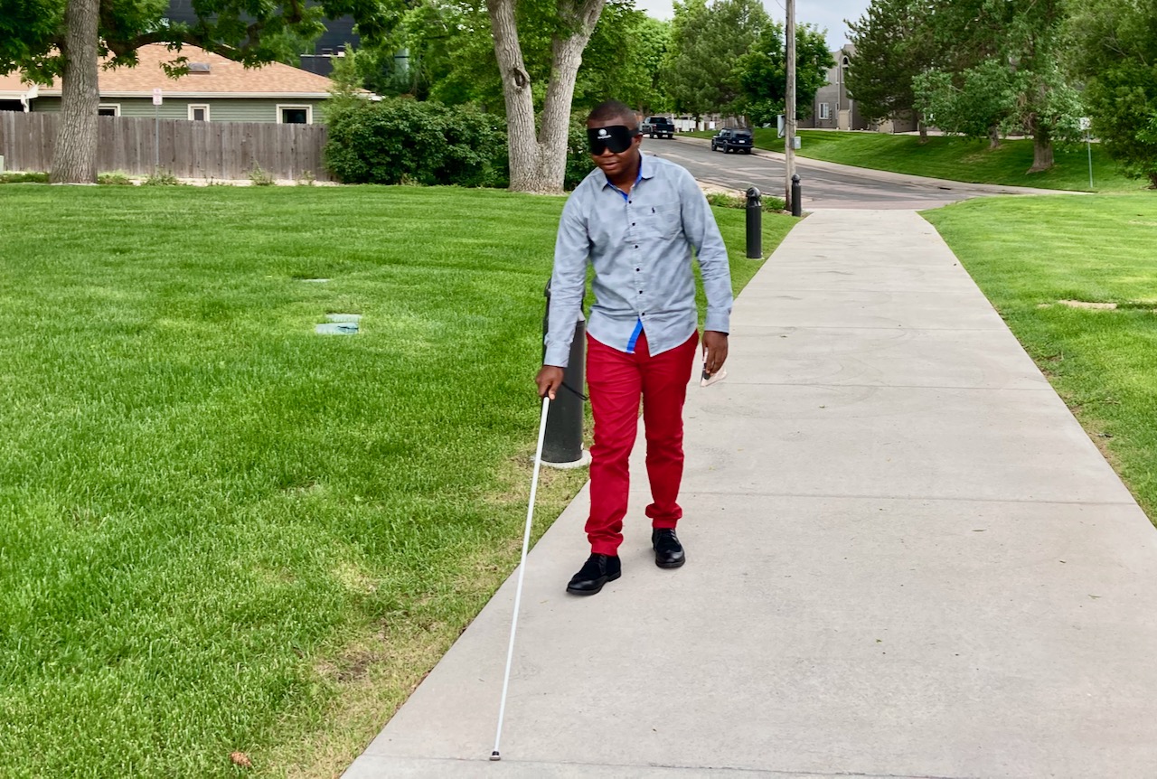 a man in red pants and learning shades uses his cane to walk up the sidewalk