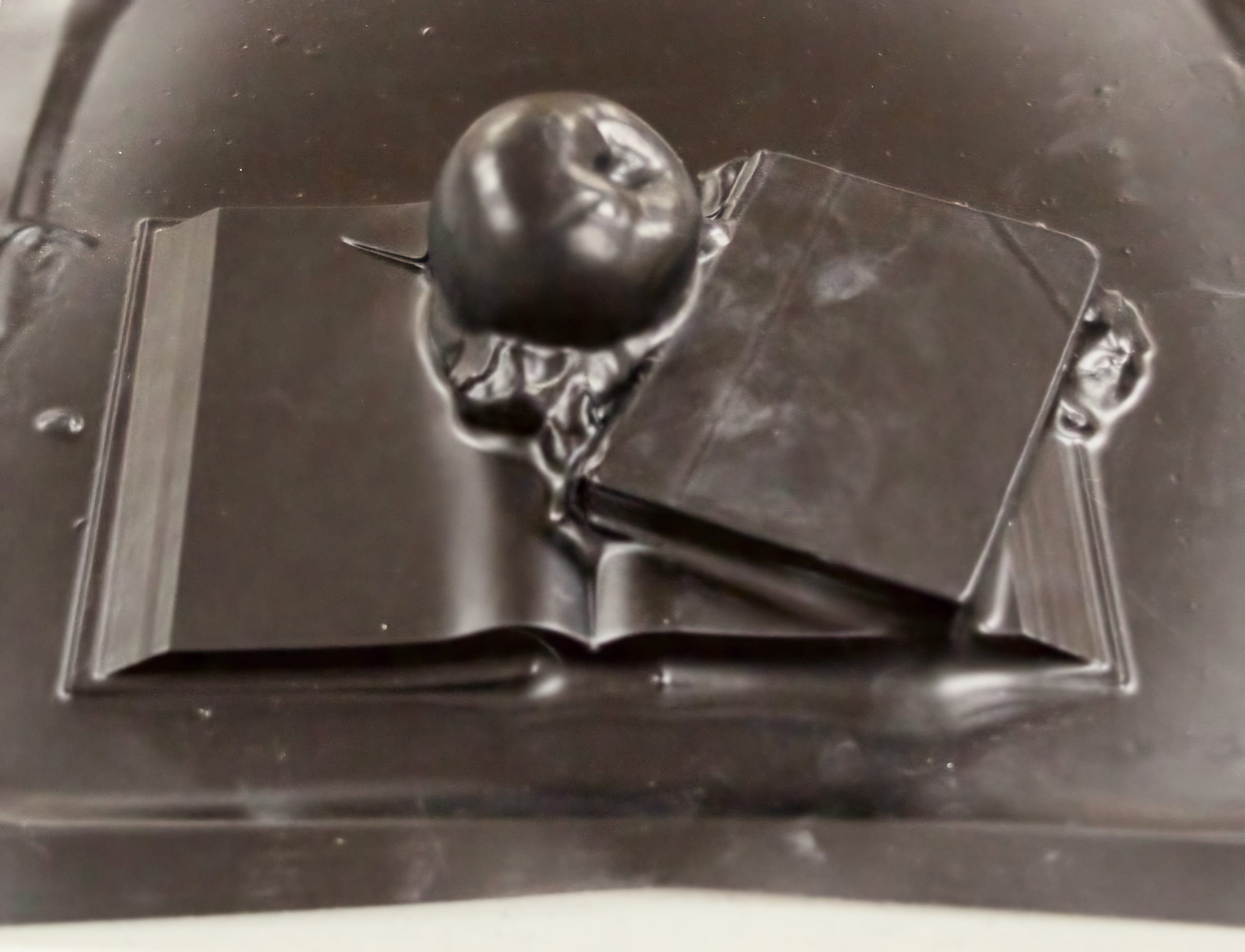 A black plastic sheet impressed with an apple atop one open and one closed book