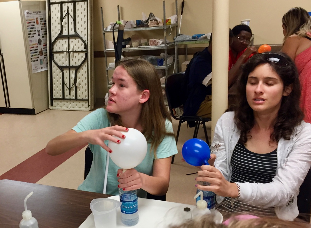 Maggie and Lauren watch as their experiment produces gas that inflates balloons
