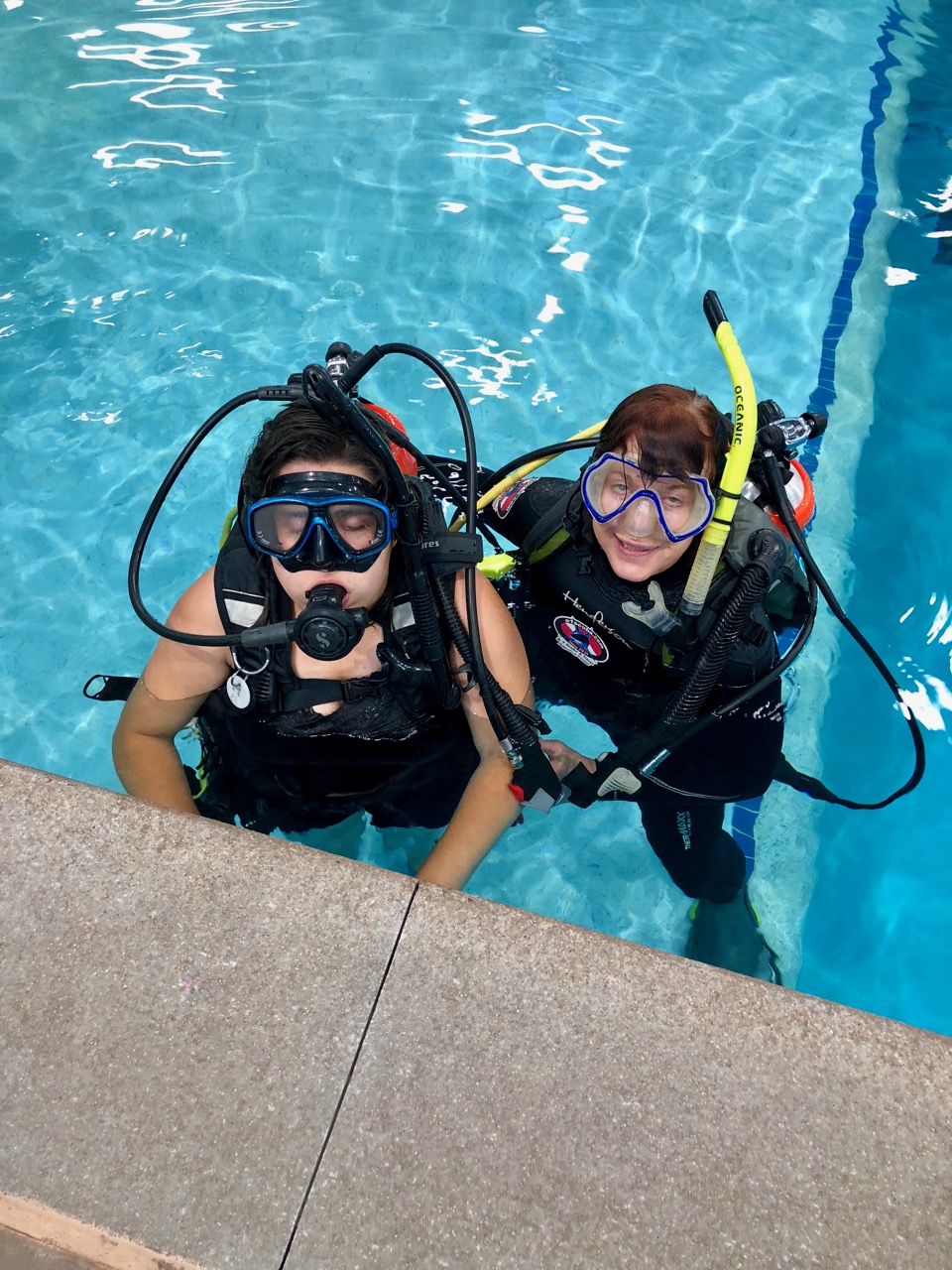 Two women at the surface of a pool with diving masks pushed onto their foreheads